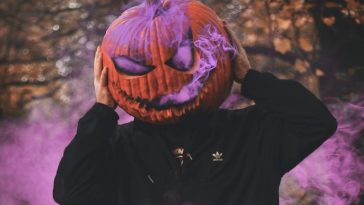 Man surrounded by purple smoke with pumpkin on his head.